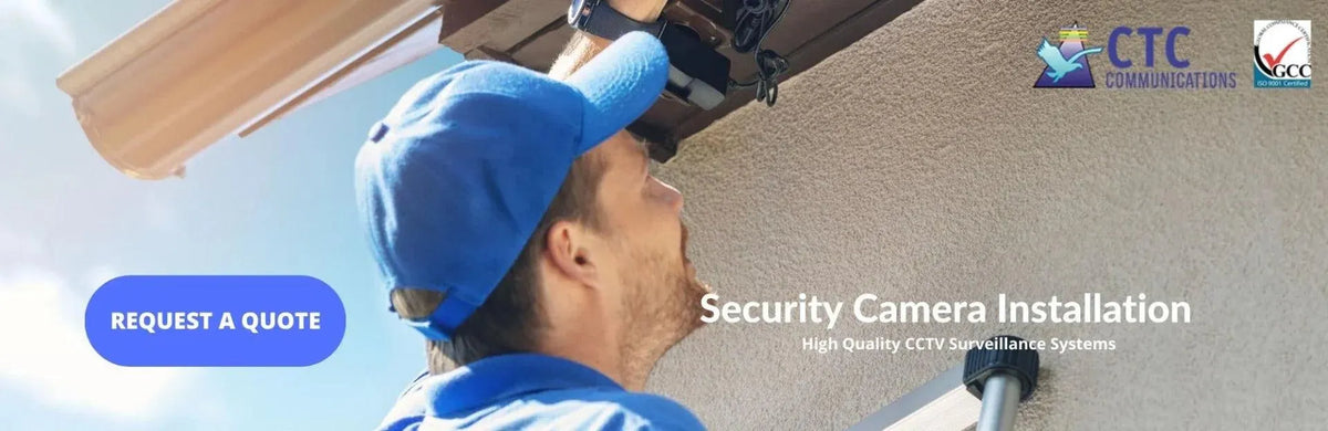 Technician in a blue cap professionally installing a dark security camera under a building's eaves.